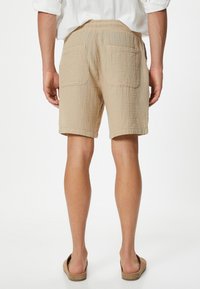 Shorts in cotone beige con una texture stropicciata, cintura elasticizzata e due tasche posteriori. Orlo delle gambe rifinito e vestibilità rilassata.