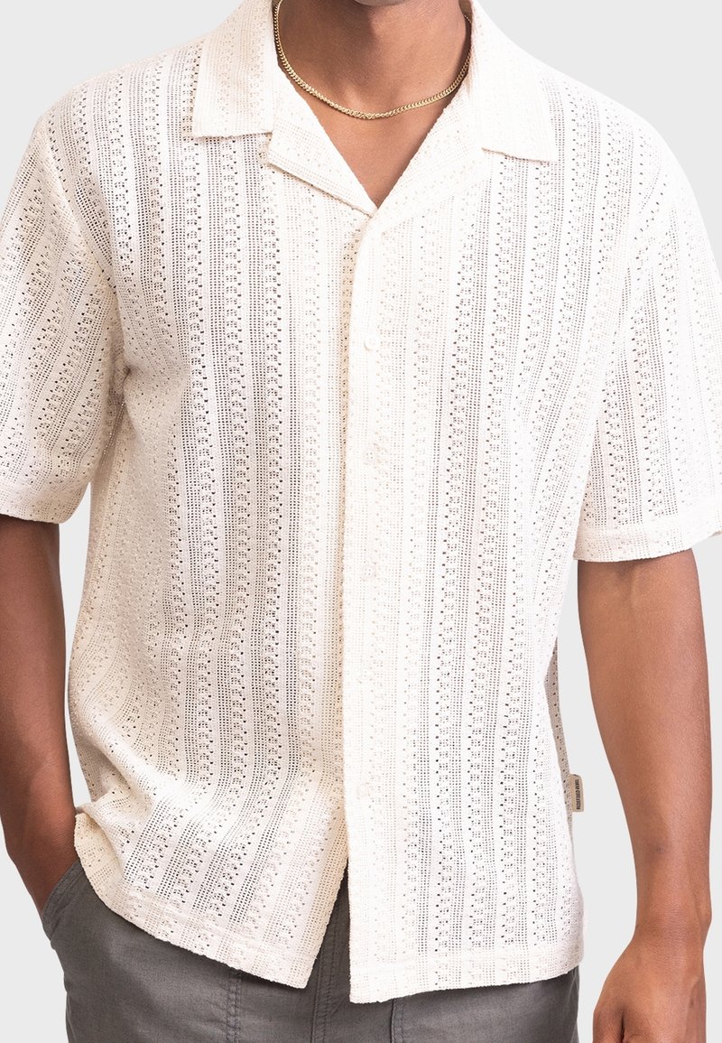 White short-sleeve shirt featuring a textured knit pattern with vertical stripes and an open collar, buttoned, and lightly relaxed fit.