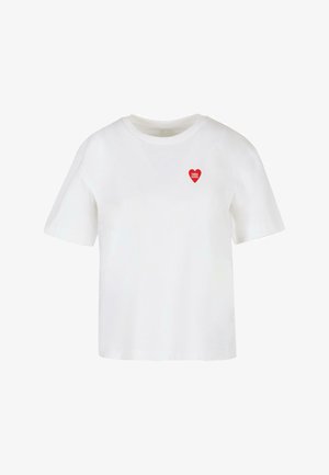 Valkoinen puuvillapaita, jossa on lyhyet hihat, pyöreä kaula-aukko ja punainen sydängrafiikka, jonka sisällä on painatus "TRÈS COOL".