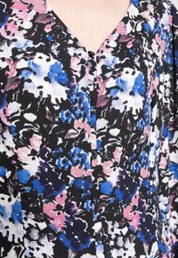 Blusa floral com decote em V, fundo preto com padrões em rosa, azul e branco. Detalhada com botões na parte da frente. Tecido suave.