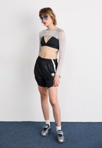 Black athletic shorts with mesh texture, paired with a black triangular bikini top and a sheer silver long-sleeve top. Gray athletic shoes.