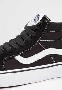 Schwarzer High-Top-Sneaker mit einem Obermaterial aus Canvas und weißen Akzenten, dicken Schnürsenkeln, Seitestreifen und einer strukturierten Gummisohle.