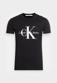 Camiseta negra de manga corta con cuello redondo, con un gran logo blanco "CK" y "Calvin Klein Jeans" centrado en la parte delantera.