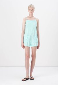 Rompers en lin bleu clair avec fines bretelles, deux poches avant et une coupe ample, avec une finition texturée et un design short.