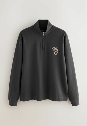 Hanorac gri cu fermoar la gât, realizat dintr-un material moale. Are mâneci lungi și un logo auriu "NYC" pe partea stângă a pieptului. Textură netedă și design minimalist.