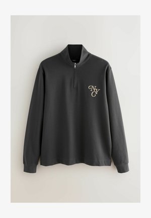 Hanorac gri cu fermoar la gât, realizat dintr-un material moale. Are mâneci lungi și un logo auriu "NYC" pe partea stângă a pieptului. Textură netedă și design minimalist.