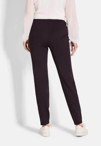 Zwarte stretchbroek met een elastische tailleband, rechte snit en een zachte textuur, gecombineerd met witte sneakers. Zicht van achteren.