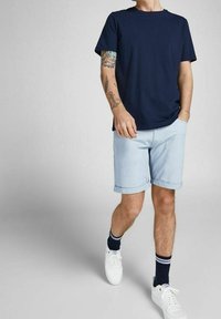 Námořnické bavlněné tričko v kombinaci se světle modrými denimovými šortkami. Bílé tenisky s tmavými ponožkami se pruhy. Jednoduchý, neformální design.