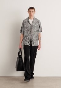 Short-sleeve patterned shirt in grey, black, and white, paired with black trousers and a black tote bag, featuring a relaxed fit and smooth texture.