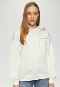 Crème hoodie met een trekkoord, met de tekst "Significant Other" op de voorkant. Zacht, ontspannen pasvorm met ribgebreide manchetten en zoom. G gedragen met een spijkerbroek.