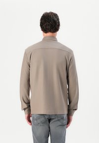 Cămașă cu mânecă lungă, de culoare khaki, cu guler, din material texturat și croială dreaptă. Vederea din spate arată linii curate și mâneci ajustate.