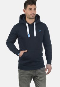 Navy blue hoodie made of cotton blend, featuring white drawstrings, front pocket, and subtle logo on the chest. Regular fit and long sleeves.