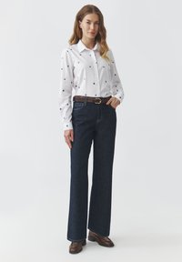 Witte overhemd met blauwe stippen, donkerblauwe wijde jeans, bruine riem en bruine enkellaarsjes. Eenvoudig, schoon ontwerp.