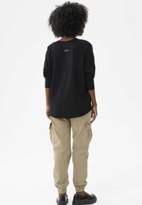 T-shirt noir surdimensionné à manches longues, ourlet arrondi, avec une petite étiquette à l'arrière. Associé à un pantalon cargo kaki et des chaussures noires.