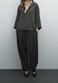 Haut oversize gris foncé avec col retourné et détail de nœud, associé à un pantalon noir ample. Tissu à texture lisse et coupe décontractée.