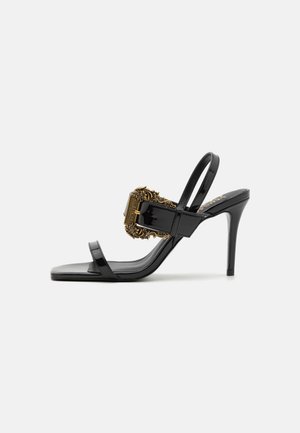 Sandalo con tacco alto in pelle verniciata nera, dotato di una preziosa fibbia dorata. Presenta due fasce sottili e un design elegante e aperto.
