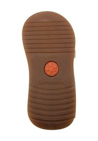 Brun gummisula med vertikala spår, en cirkulär orange accentknapp och präglad text "biomekanik". Slät yta överlag.