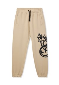 Beżowe dresy wykonane z miękkiego materiału, z elastycznym paskiem w talii z sznurkiem, bocznymi kieszeniami oraz czarnym graffiti na udzie.