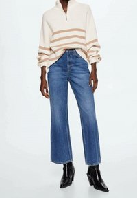 Pull crème avec des rayures beige horizontal, col zippé mi-hauteur, associé à un jean bleu taille haute et large et des bottines noires.