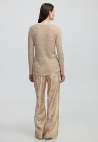 Beige Strickoberteil mit langen Ärmeln und strukturiertem Muster, kombiniert mit hellgoldbraunen, weit geschnittenen Hosen mit dezentem Blumendesign.