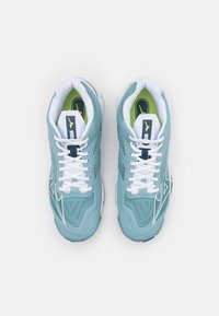 Ljusblå sportskor med vita snören, meshöverdel, texturerad design och gröna accenter på innersulorna och tungan.