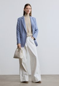 Ανοιχτό γαλάζιο σακάκι προσαρμοσμένης κοπής, μπεζ ζιβάγκο, άσπρο παντελόνι με φαρδιά μπατζάκια, μπεζ τσάντα με στρογγυλή λαβή, απαλές υφές και καθαρές γραμμές.