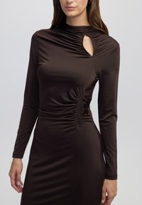 Braunes Langarmkleid mit geraffter Textur, das eine Schlüssel-Ausschnittöffnung am Ausschnitt und eine taillierte Silhouette aufweist. Glattes, dehnbares Material.