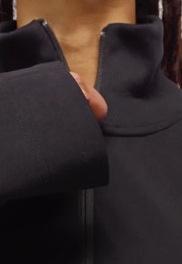 Crna jakna sa zipom na prednjoj strani koja ima visoki ovratnik i manžete na rukavima, napravljena od glatkog, rastezljivog materijala s vidljivim detaljima šivanja.