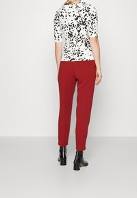 White top with black splatter pattern, paired with red pants. Black, heeled ankle boots complete the outfit.  Casual design, fitted silhouette.