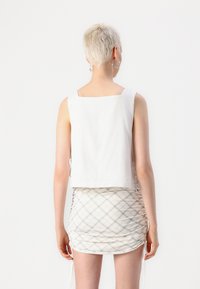 White cropped tank top with square neckline paired with a ruched, plaid mini skirt. The skirt features drawstring accents at the sides.