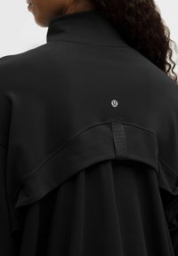 Čierny pulóver s vysokým golierom, ktorý má vrstvený dizajn na zadnej strane. Hladká textúra a logo značky v strede blízko výstrihu.