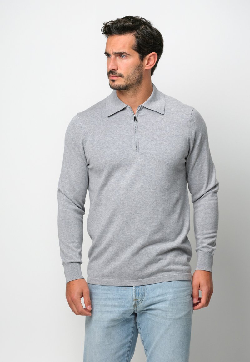 Graues Langarm-Polohemd mit Reißverschluss vorne und flachem Kragen, aus weichem Stoff, kombiniert mit hellblauen Jeans.