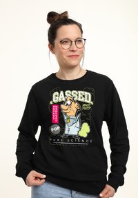 Svart sweatshirt med en grafisk cartoonfigur och text. Designen inkluderar gröna accenter och ett lekfullt tema som kretsar kring vetenskap.