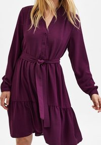 Lila klänning med långa ärmar, knapad front, knytmidja och flikad nederdel. Slät textur med en mjuk lyster, med en avslappnad passform.