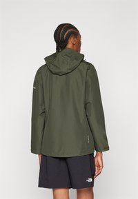 Grønn vanntett jakke med hette, med en jevn tekstur, elastiske mansjetter og en litt løs passform, kombinert med svarte shorts.