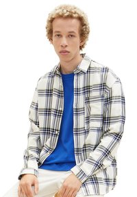 Langeærmet ternet skjorte i hvid, blå og grøn med knaplukning. Båret over en blå t-shirt. Har en afslappet pasform og en brystlomme.