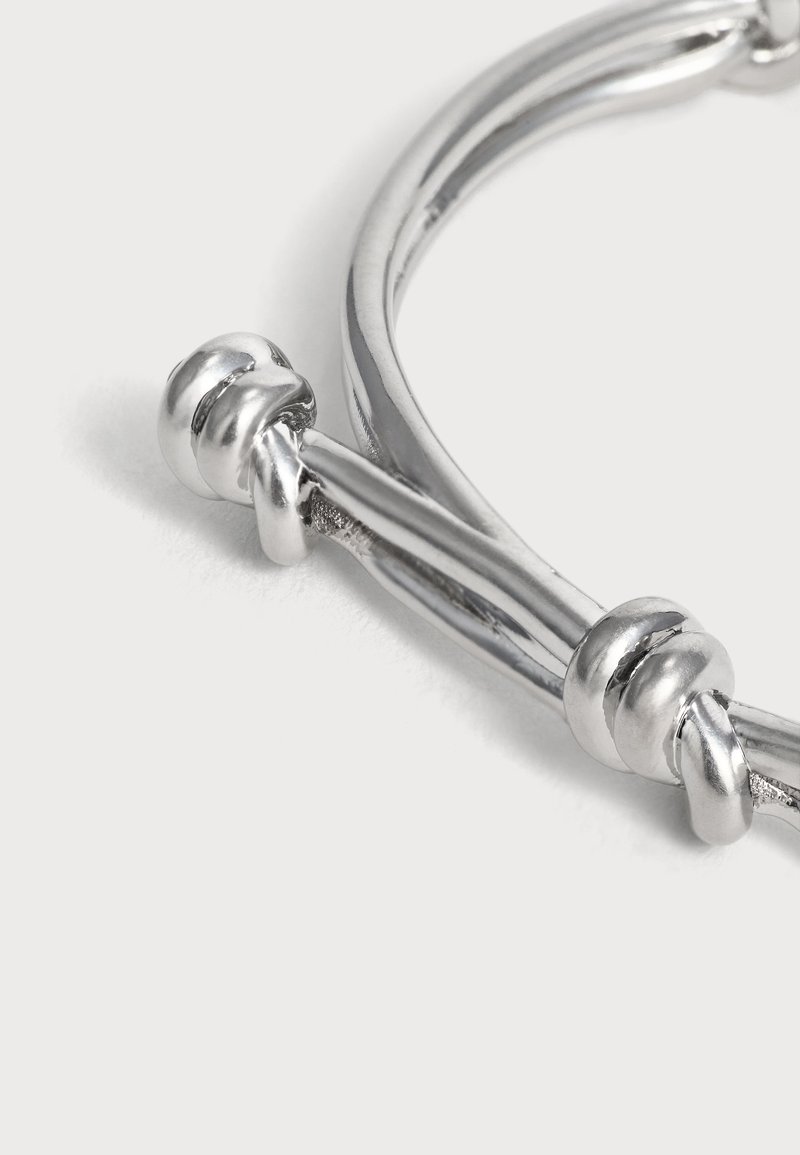 Glanzende zilveren armband met een gladde afwerking, voorzien van decoratieve knopen die gelijkmatig over de gebogen band zijn verdeeld.