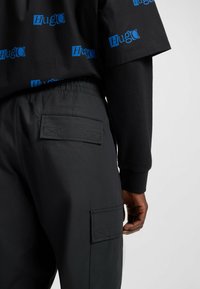 Zwarte korte mouwen shirt met blauwe "Hugo" logo, gecombineerd met zwarte cargo broek met zakken en een gestructureerde stof.