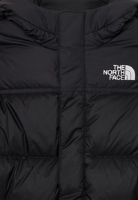 Črna puffer jakna z vidnim šivanjem in belim vezenim logotipom "The North Face" na zgornjem desnem predelu prsnega koša.
