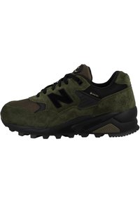 Zapatillas deportivas de ante verde y malla con acentos negros, que cuentan con una suela de goma gruesa y un prominente logo "N" en el lateral.