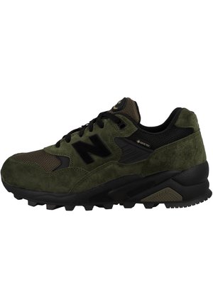 Zapatillas deportivas de ante verde y malla con acentos negros, que cuentan con una suela de goma gruesa y un prominente logo "N" en el lateral.