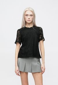 Μαύρη τοπ με δαντέλα και κοντά μανίκια, με εσοχή στον λαιμό και υφή, συνδυασμένη με γκρι φούστα πλισέ.