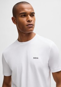 Hvit bomulls t-skjorte med rund hals og korte ermer, med en liten svart "BOSS"-logo på venstre bryst.