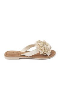 Infradito beige con una soletta testurizzata color tan e ampie cinghie bianche. Un dettaglio floreale di un leggero color crema decora la parte superiore.