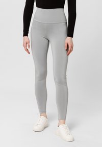 Leggings a vita alta di colore grigio chiaro realizzati in materiale elasticizzato, con una texture liscia e un design aderente. Indossati con sneakers bianche.