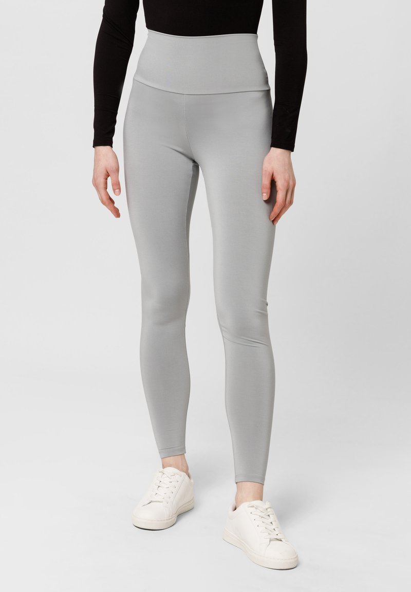 Leggings a vita alta di colore grigio chiaro realizzati in materiale elasticizzato, con una texture liscia e un design aderente. Indossati con sneakers bianche.