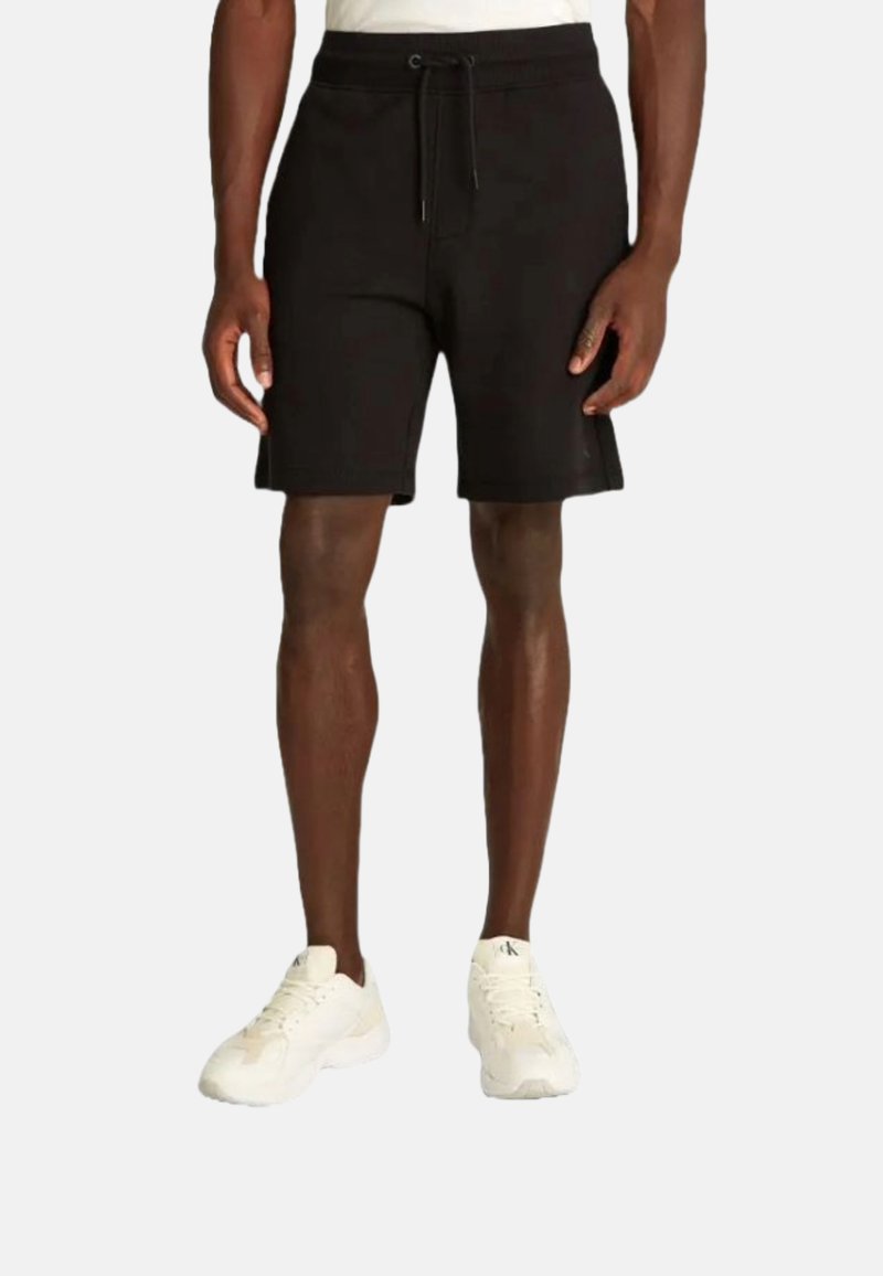 Pantaloni corti neri in cotone con cintura elastica e cordino, dotati di tasche laterali e orlo dritto, indossati con sneakers bianche.