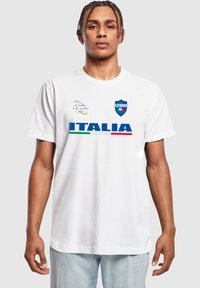 Balta medvilninė marškinėliai su užrašu "ITALIA" mėlyna spalva, su žaliais ir raudonais dryžiais; taip pat yra "AZZURRO" logotipas ir tekstas mėlyna bei auksine akcentų spalva.