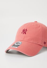 Gorra de béisbol de algodón rosa con logotipo NY bordado en rojo oscuro, correa ajustable y visera texturizada. Presenta una etiqueta circular de la marca 47.