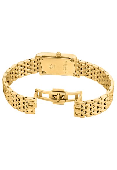 Zlatý kovový náramkový hodinky s obdélníkovým pouzdrem, spojeným náramkem a zapínáním na sponu. Na zadní straně jsou vyryté údaje o značce.